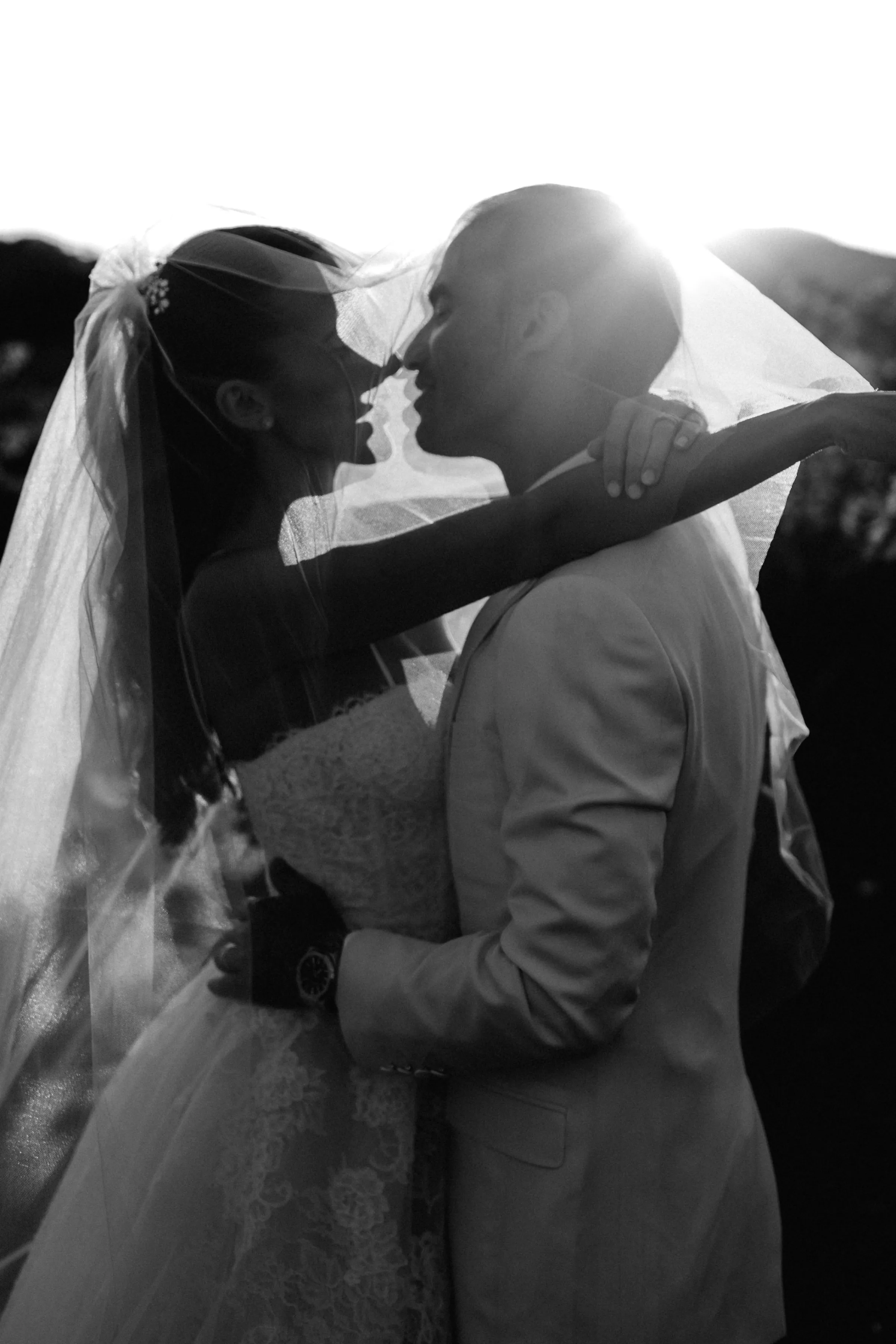 Les mariés s’embrassent sous le voile à contre-jour, photo noir et blanc