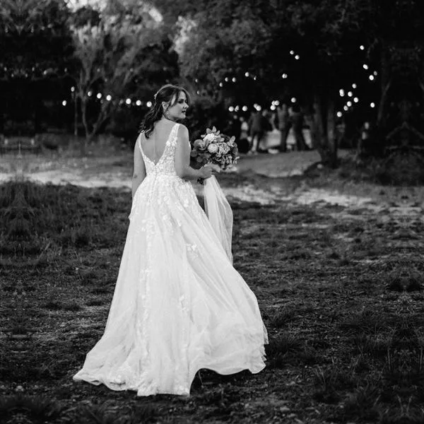 Mariée de dos rejoignant ses invités sous les guirlandes lumineuses, photo noir et blanc