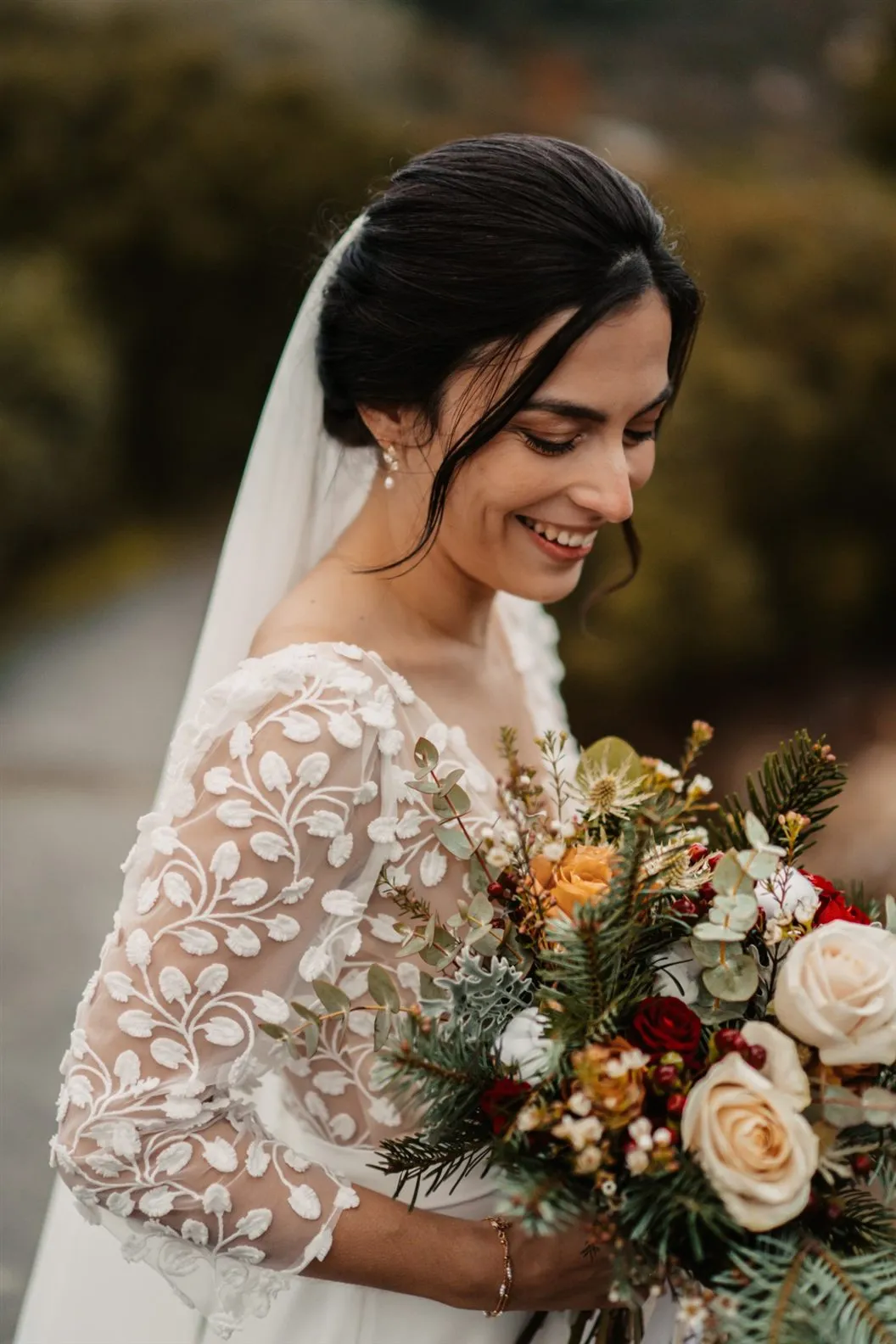 Mariée souriante en robe de dentelle avec son bouquet d’hiver