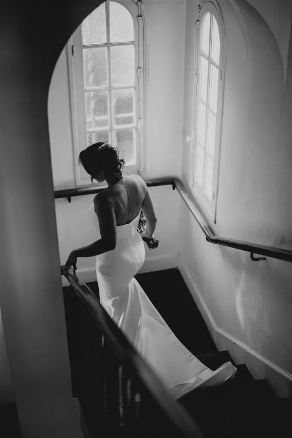 Mariée descendant un escalier sous de grandes fenêtres, photo noir et blanc