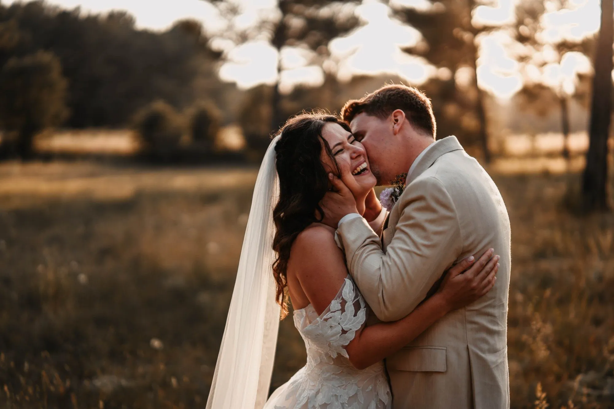 Le marié embrasse la joue de la mariée qui éclate de rire, golden hour en Provence