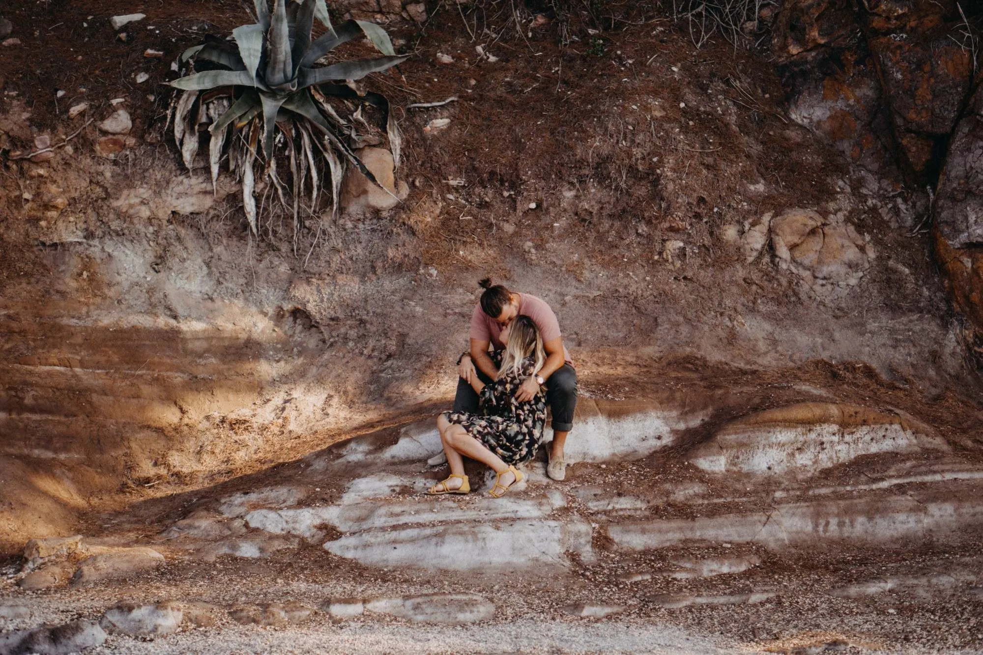 Séance couple : les amoureux s’embrassent, assis sur les rochers sous un agave