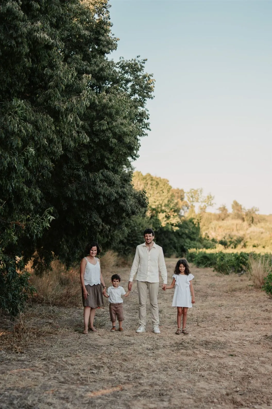 Séance photo famille dans un chemin bordé de vignes, parents et enfants main dans la main